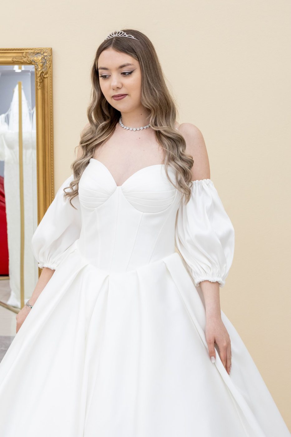 Mireasă în rochie din satin cu mâneci bufante, lângă oglinda aurie