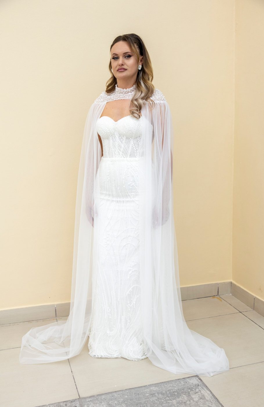 Mireasă în rochie mulată brodată cu perle și capă lungă din tul, în showroom